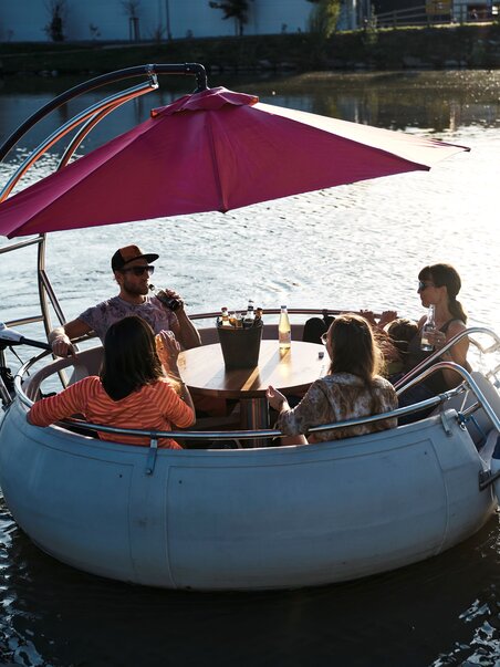 Gruppe von Freunden in einer Murgondel - das ist ein rundes Boot - auf der Mur bei Sonnenuntergang. | © Stadtstrand Graz - Stefan Leitner