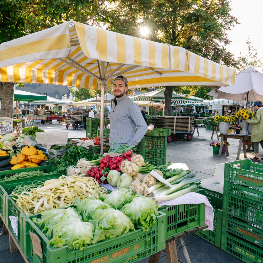 Scena di mercato vivace con verdure fresche e venditore a Graz. | © Graz Tourismus - Mias Photoart