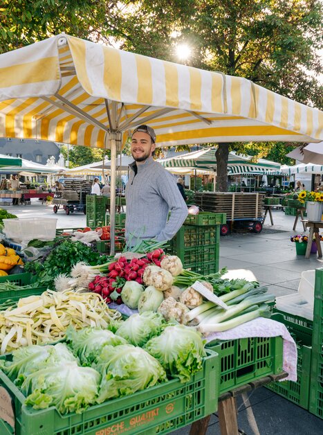 Vibrant market scene with fresh vegetables and seller in Graz. | © Graz Tourismus - Mias Photoart