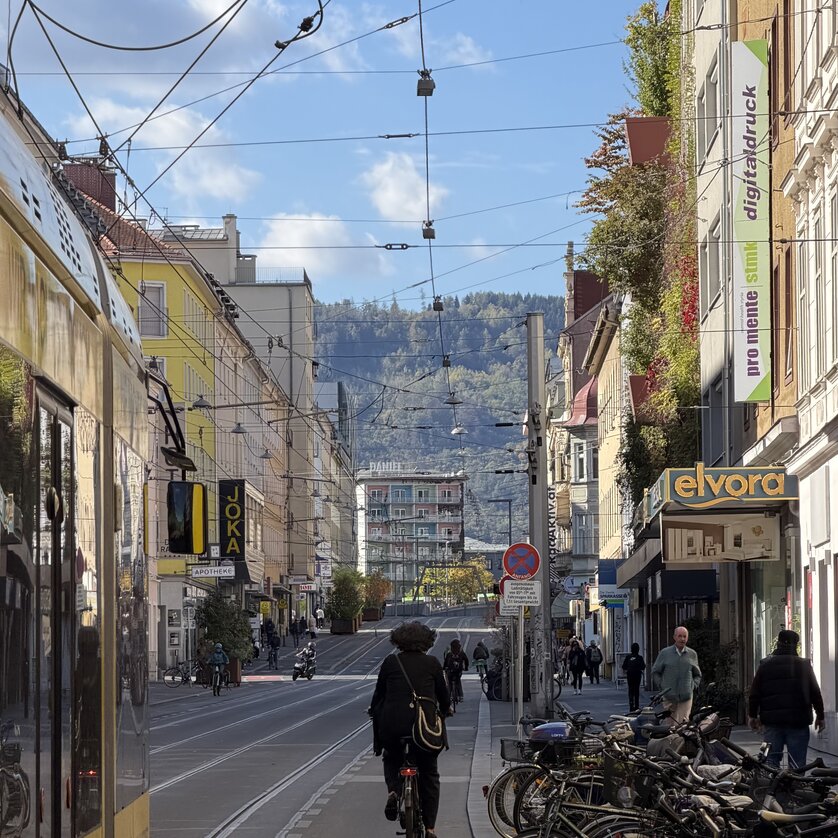 Straße in Graz mit Fahrradfahrer, Geschäften und Blick auf die Berge. | © Graz Tourismus