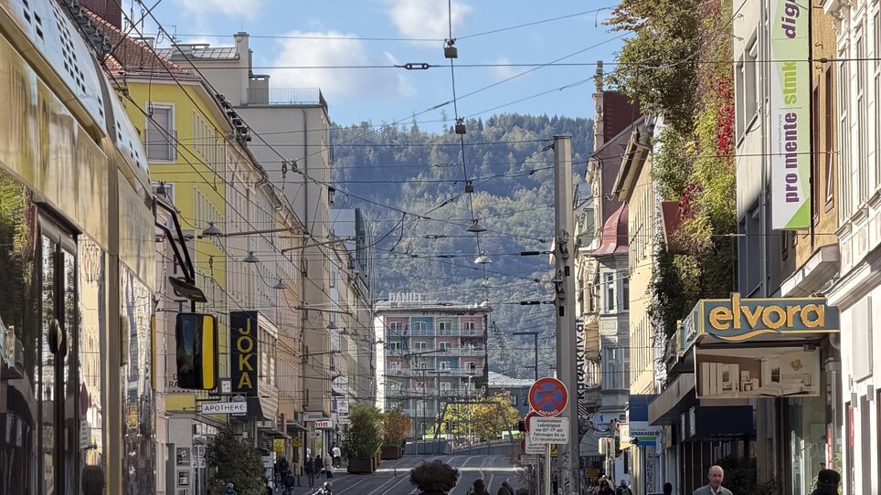 Straße in Graz mit Fahrradfahrer, Geschäften und Blick auf die Berge. | © Graz Tourismus