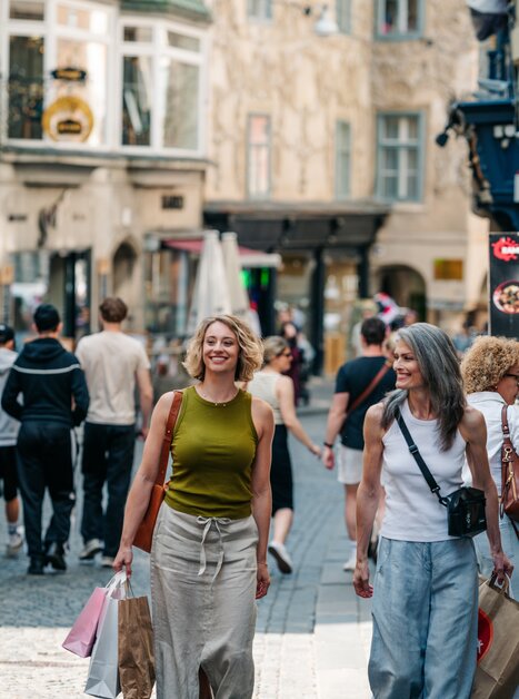 Zwei Frauen gehen fröhlich in Graz mit Einkaufstüten an einem belebten Tag spazieren. | © Graz Tourismus - Mias Photoart