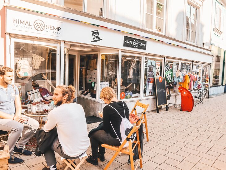 Three people are sitting in front of a shop in the Lendviertel neighbourhood in Graz. | © Janet Newenham - Journalist On The Run