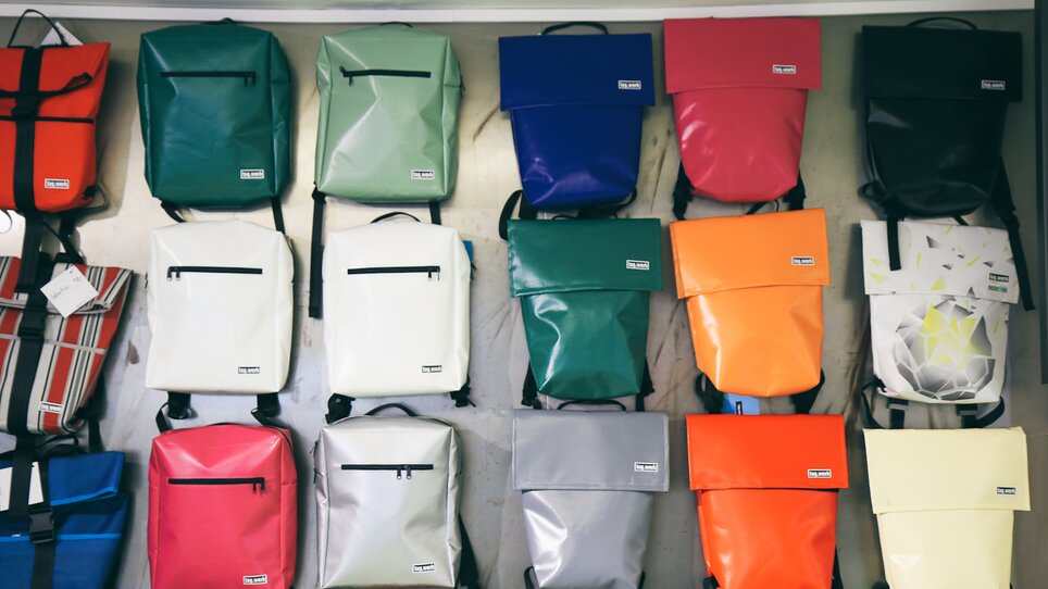 Bunte Rucksäcke in verschiedenen Farben an einer Wand. | © Nina Hüpen-Bestendonk