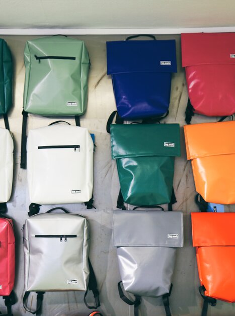 Colorful backpacks of various colors hanging on a wall. | © Nina Hüpen-Bestendonk
