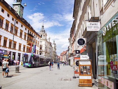 Vista di una strada affollata a Graz con negozi e tram. | © sFachl