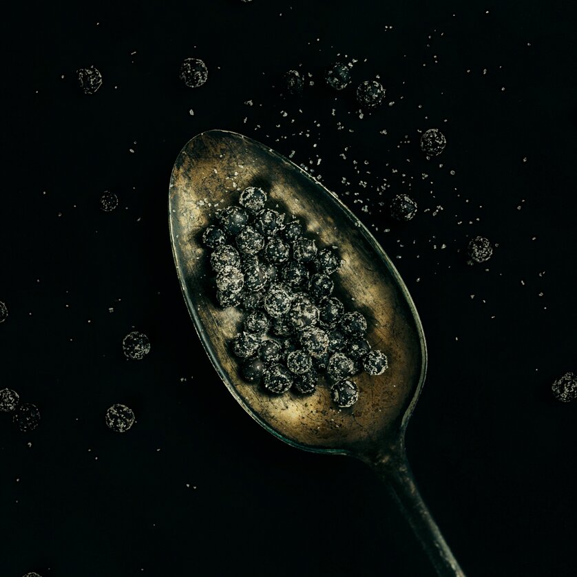 Ein Löffel voll dunkler Pfefferkörner auf schwarzem Hintergrund. | © Lupi Spuma