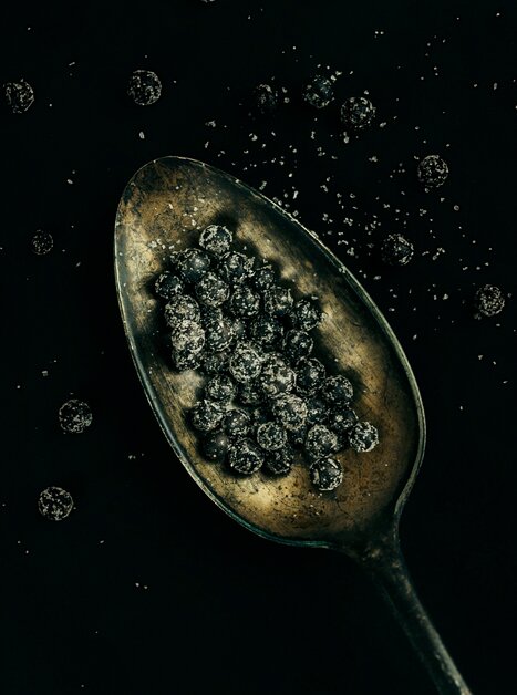 Ein Löffel voll dunkler Pfefferkörner auf schwarzem Hintergrund. | © Lupi Spuma