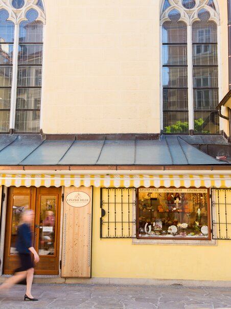 Eine Person geht an einem Geschäft in Graz vorbei, mit schönen Fenstern und einer gelben Fassade. | © Graz Tourismus - Harry Schiffer