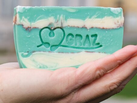 Una mano tiene un pezzo di sapone con 'I❤️GRAZ' a Graz. | © tinksi
