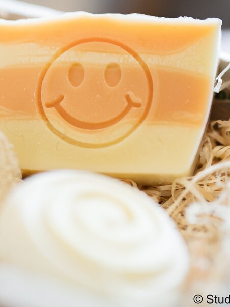 Sapone colorato con un volto sorridente e un sapone a spirale sullo sfondo. | © Studio Lou