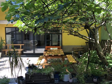 Ein schöner Innenhof mit einem Holz-Tisch unter einem Baum, umgeben von Pflanzen. | © heidenspass