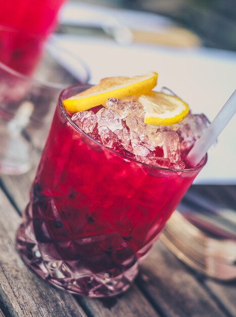 Ein roter Cocktail mit Eis und Zitronenscheiben auf einem Holztisch. | © Pixabay