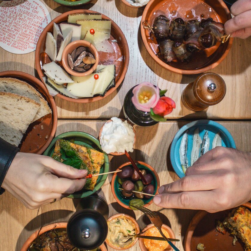 Tisch mit verschiedenen Tapas und Getränken, Hände greifen nach Snacks. | © Cielo Graz