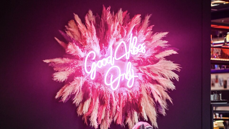 Interno elegante con luce al neon 'Good Vibes Only' e opzioni di posti a sedere accoglienti. | © Bonbon