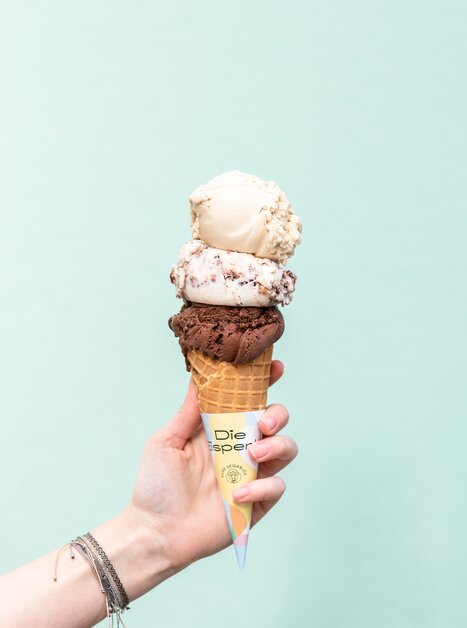 Eine schmackhafte Eistüte mit drei Kugeln Eis in verschiedenen Geschmacksrichtungen vor einem mintgrünen Hintergrund. | © Eisperle - Stiefkind Fotografie