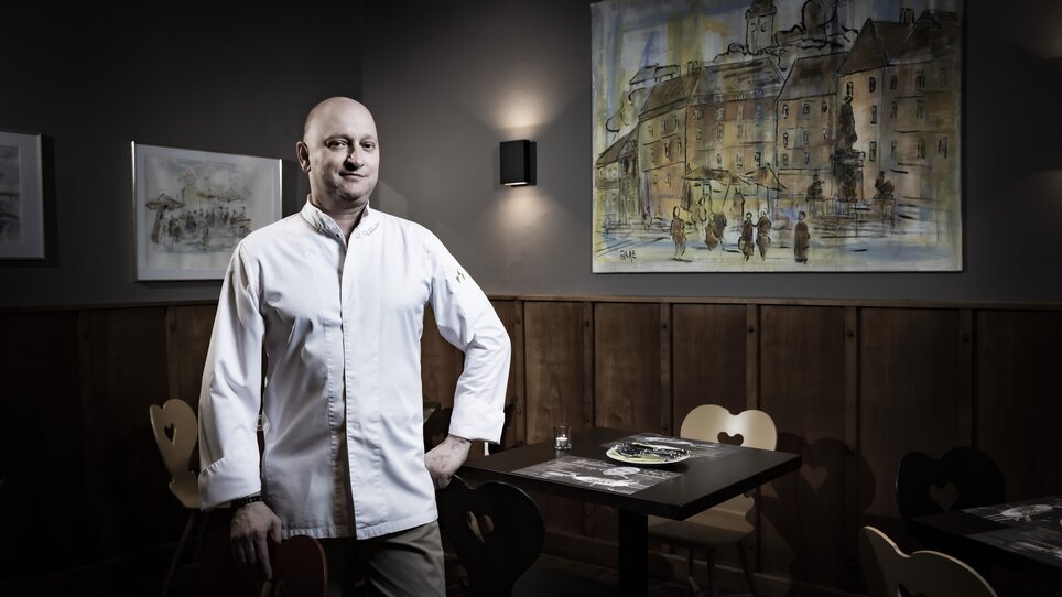 A chef stands in a restaurant with a painting in the background. | © Graz Tourismus - Werner Krug