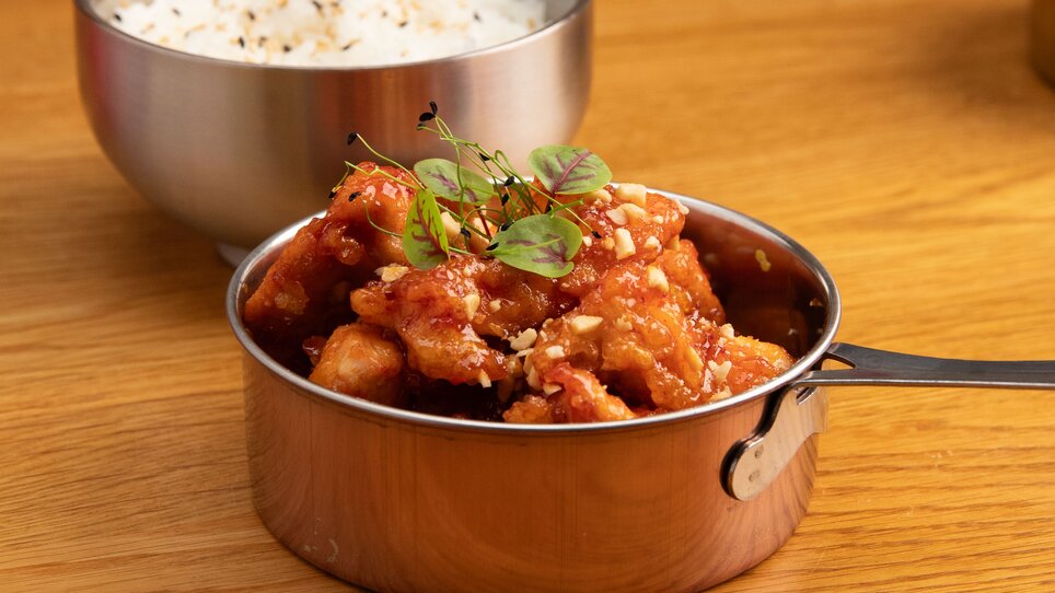 Una ciotola argentata con pollo dolce e riso, servita su un tavolo di legno. | © Gogi KG