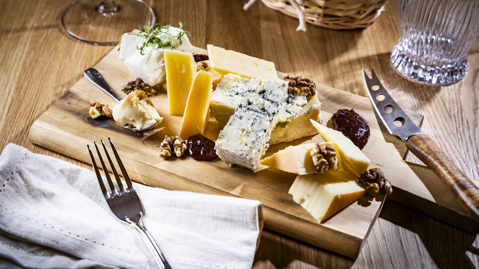 A wooden board featuring various cheeses, nuts, and jam. | © Kaiser Greissler - Werner Krug