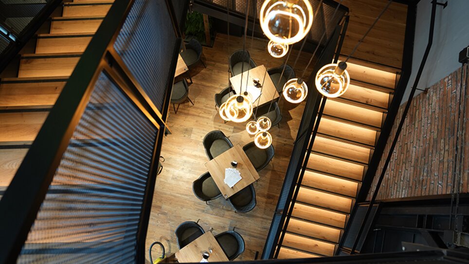 Moderner Restaurantbereich mit Holztischen und hängenden Lampen. | © The Guardians