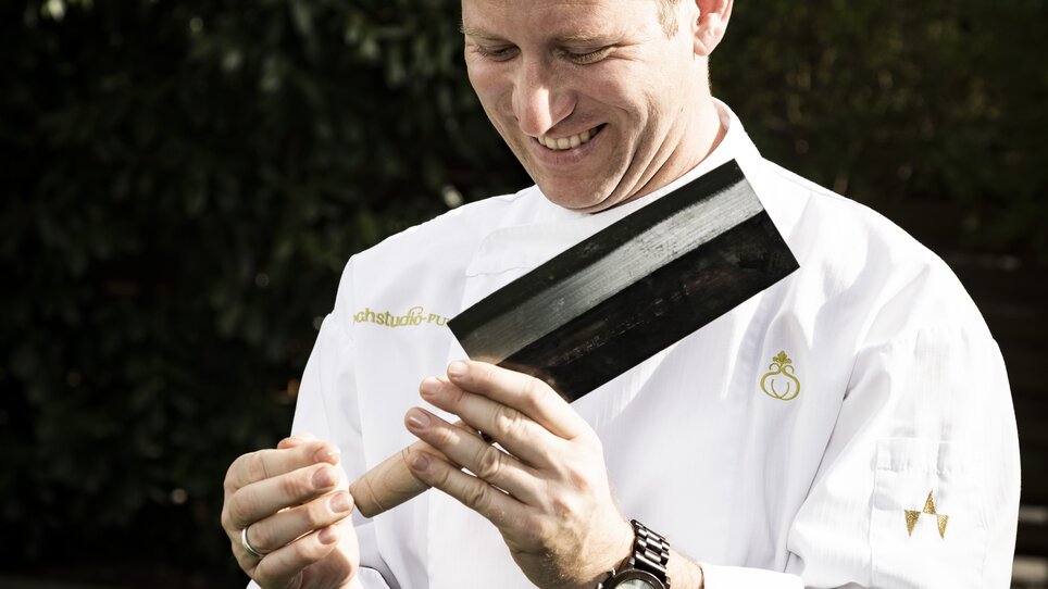A smiling chef examines a large cooking knife. | © Werner Krug