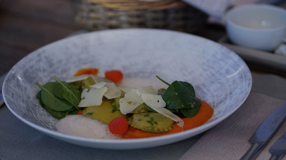 A refined plate featuring ravioli, spinach, tomatoes, and parmesan. | © aiola