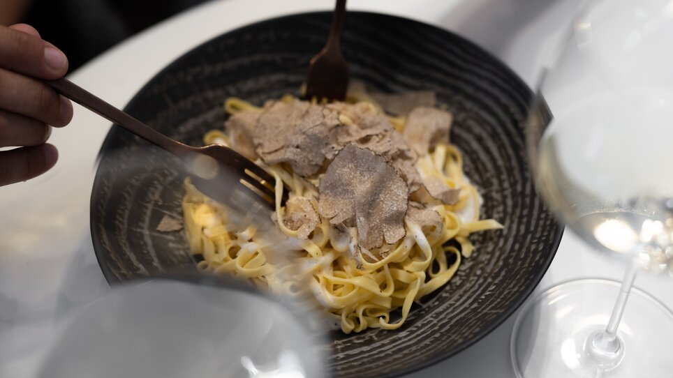 Pasta with truffles in a bowl, surrounded by wine glasses. | © Auenbrugger