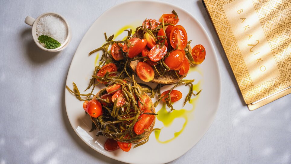 Un piatto con pomodori freschi, erbe e pane, accanto a una tazza di sale. | © Muamer Gazibegovic 1)