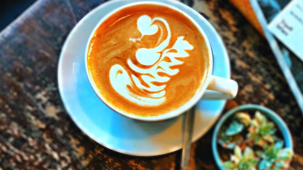 Un delizioso caffè con schiuma di latte in una tazza su un tavolo di legno. | © Beanery