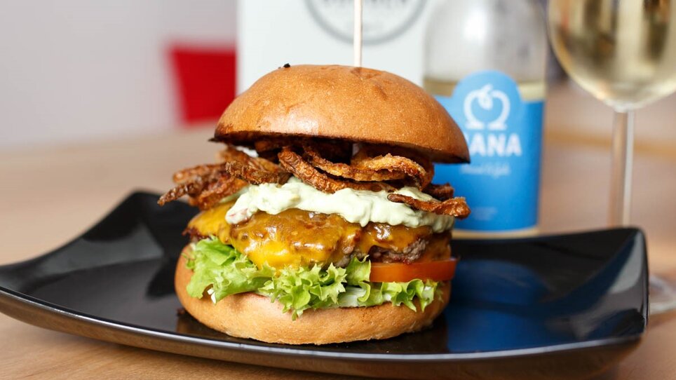Saftiger Burger mit Käse, Salat und Zwiebelringen auf einem Teller. | © Burger Factory