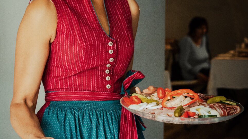 Woman carries two plates of fresh dishes, smiling warmly. | © Buschenschank Hildebrand