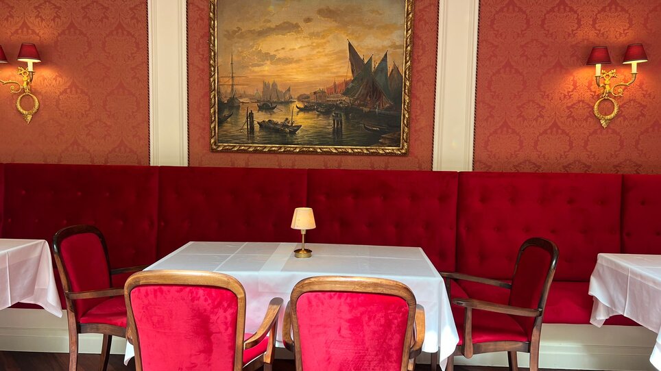 Elegant restaurant with red walls, tables, and a piece of artwork. | © Café Herzog