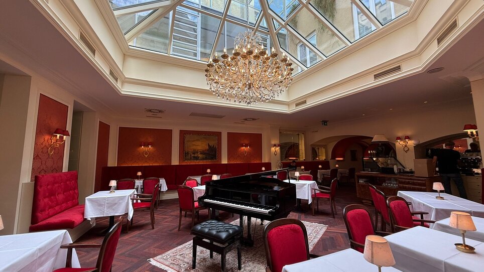Elegant café with piano, chandelier, and glass roof. | © Café Herzog
