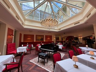 Elegantes Café mit Klavier, Kronleuchter und Glasdach. | © Café Herzog
