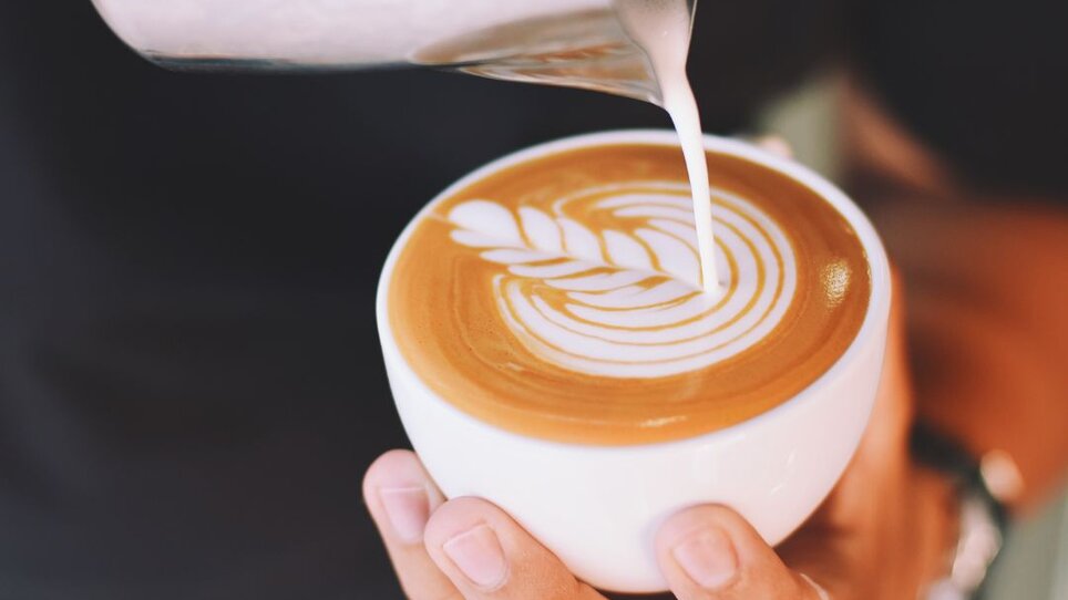 A person pours milk into a cup of coffee. | © Café Muhr