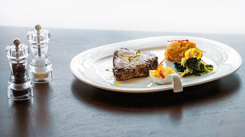 Ein Teller mit mariniertem Fisch, Beilagen und Gewürzmühlen. | © Michael Fiedler