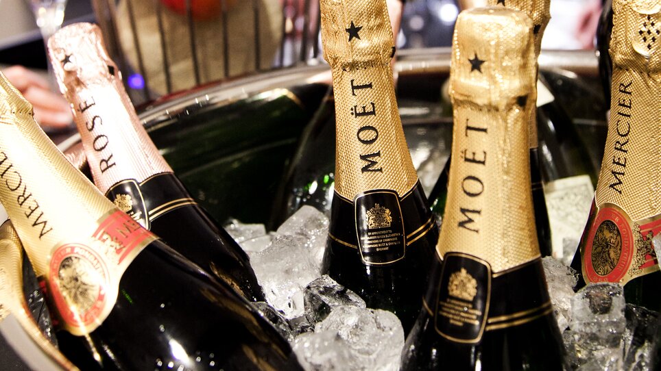 Champagner Flaschen in einem Weinkühler mit Eiswürfeln, mit Obst im Hintergrund. | © Tageskaffee Freiblick 