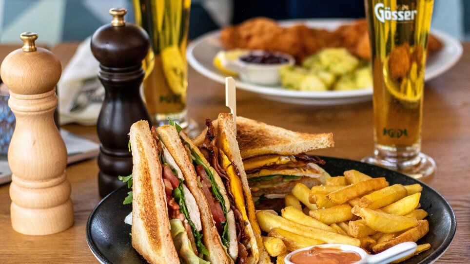 A delicious sandwich with fries and drinks on a table. | © Das Franz