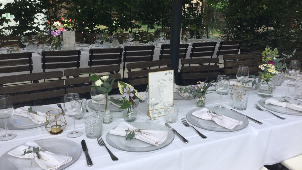 Elegant gedeckter Tisch für ein Event im Freien, mit Blumen und Menükarten. | © Das Lorenz