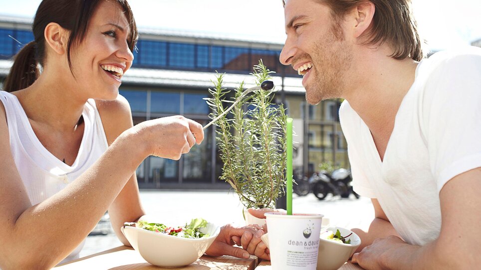 Coppia sorridente che gode di insalate e bevande all'aperto. | © dean&david