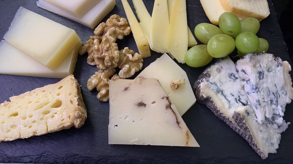 Eine Käseplatte mit Walnüssen und Trauben auf einem schwarzen Brett. | © Nussbaumer