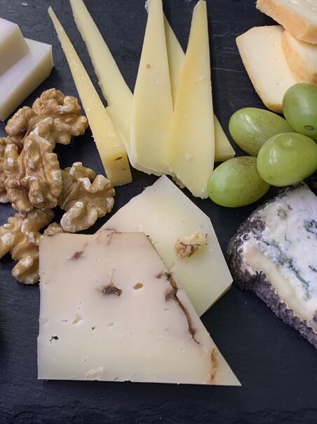 A cheese platter with walnuts and grapes on a black board. | © Nussbaumer