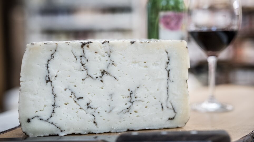 Ein Stück Käse, daneben ein Glas Rotwein und eine Flasche. | © Nussbaumer