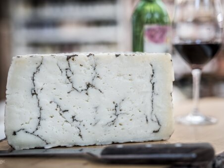 A piece of cheese, alongside a glass of red wine and a bottle. | © Nussbaumer
