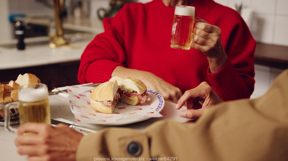 Una donna in maglione rosso con birra e panino a Graz. | © Florian Weitzer Hotels und Restaurants
