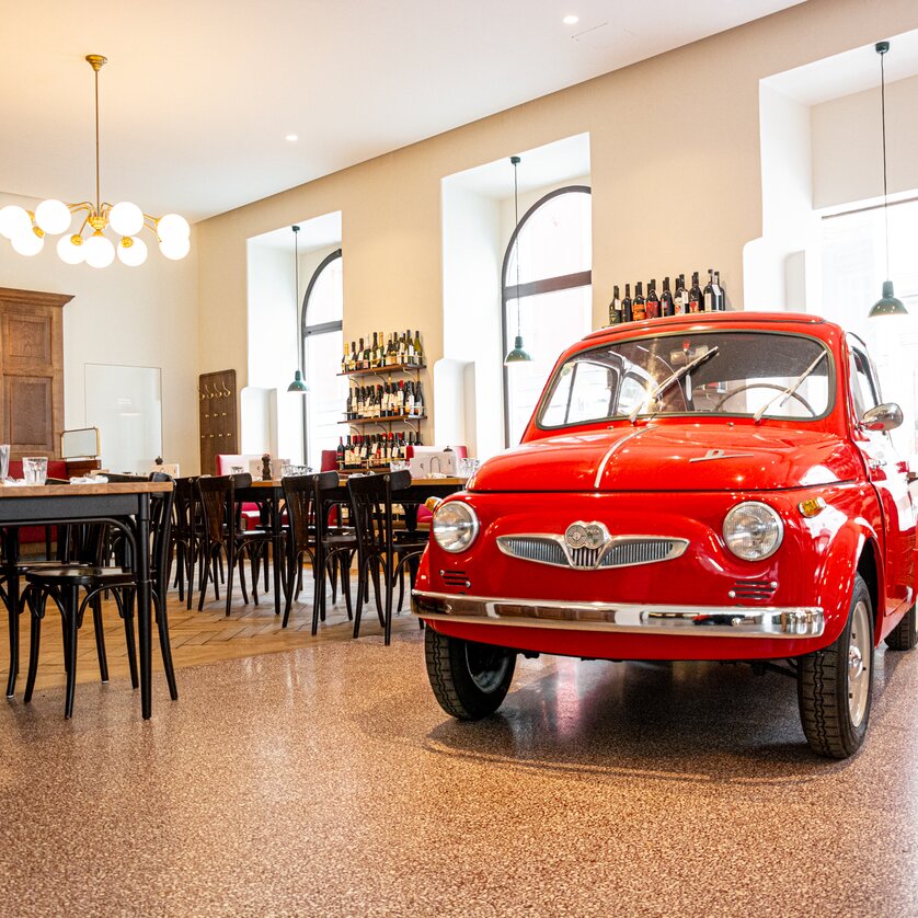 Un'auto rossa si trova nel ristorante Der Steirer a Graz, circondata da tavoli e sedie. | © Florian Weitzer Hotels & Restaurants