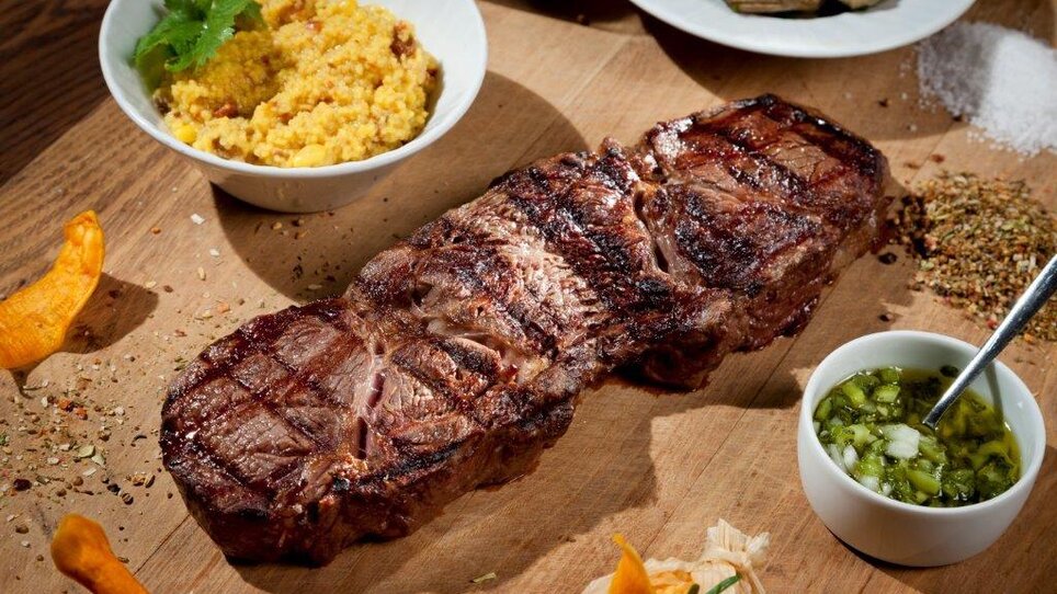 Juicy steak on wooden board, accompanied by side dishes. | © El Gaucho