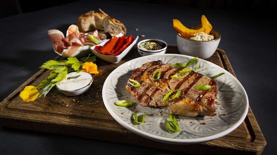 Grilled steak with sides on a wooden platter. | © El Gaucho - Werner Krug