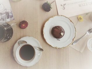 Schwarzer Kaffee und Süßgebäck auf einem Tisch, umgeben von Blumen. | © Cafe Greenhouse