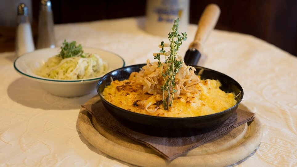 A dish topped with cheese, garnished with onions and thyme, served with a salad. | © Glöckl Bräu